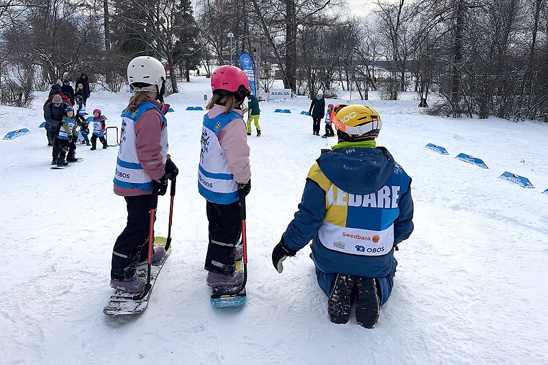 Två små barn testar snowboard med ledare från Alla på snö.